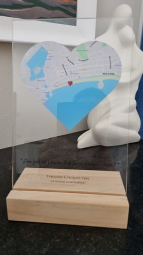 Un client montre sa plaque en acrylique personnalisée, avec une carte en forme de cœur, posée sur un socle en bois.