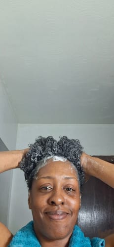 Reviewer lathering their dark curly hair with Strengthen Hair Shampoo.