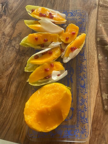 Kunde zeigt die zubereitete Bio-Keitt Mango, halbiert und als leckere Vorspeise auf einem Glasteller angerichtet.