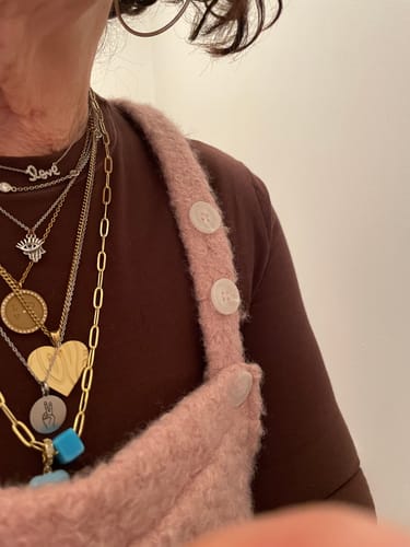 Close-up of a reviewer wearing the engraved peace sign charm as part of a layered necklace stack.