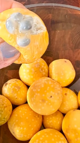 Ein Kunde zeigt das Innere einer geöffneten Baby Granadilla Lulu über einer Schale mit weiteren Früchten.