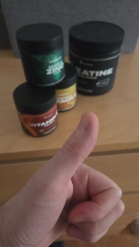 Customer gives a thumbs-up in front of their tub of Creapure Creatine, displayed with other supplements.