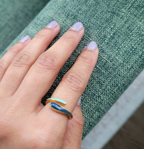 A customer's hand wearing the Safira Blue Wrap Ring on their index finger, showing its two-tone blue enamel design.
