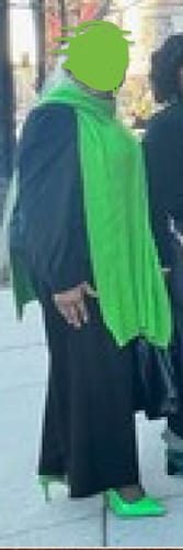 Reviewer styling the bright green asymmetric sweater with a black outfit and matching neon green heels.