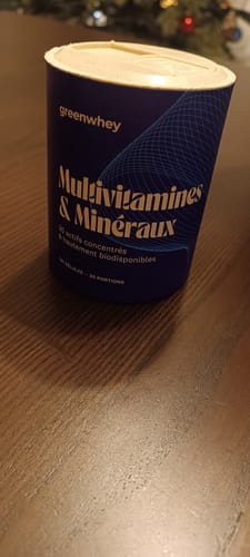 Client montrant le pot bleu des Multivitamines & Minéraux sur une table en bois.