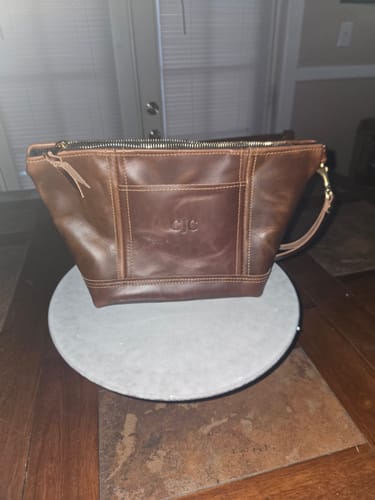 Customer's personalized brown leather Women's Toiletry Bag displayed on a table.
