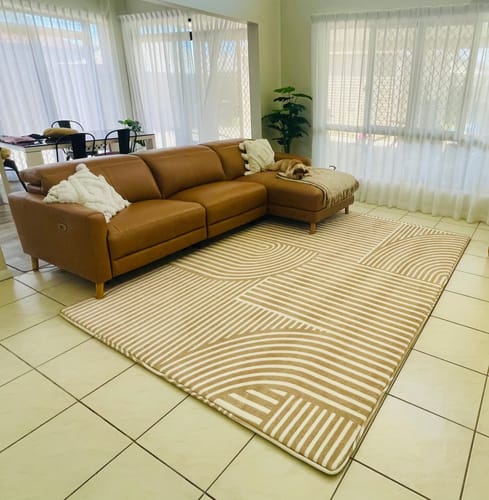 Customer's large Sahara Lines Mellow Mat with a geometric pattern placed in a living room in front of a brown sofa.