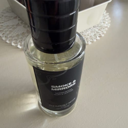 A reviewer's bottle of Smoke & Mirrors Eau de Parfum with a black label and cap, sitting on a light-colored tabletop.
