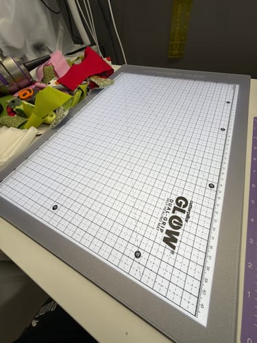 Customer's Cutterpillar Glow Premium II lightpad, illuminated on a craft table with fabric scraps nearby.