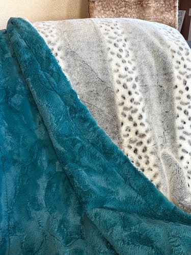 Customer's custom blanket combining a solid teal fabric and a gray and white animal print fabric, draped over a chair.