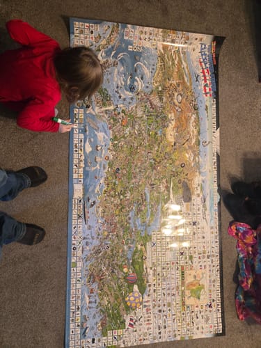 Reviewer's child lies on the floor examining the large World's Greatest Search & Discover USA Edition poster.