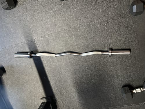 Die gebogene SZ-Curlstange eines Rezensenten liegt auf einer schwarzen Fitnessmatte.