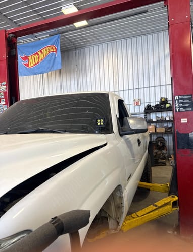Customer's white Chevy Silverado on a garage lift with the Hood Ditch Light Mounts and an LED pod light installed.