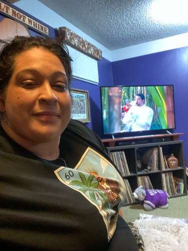 Reviewer sitting at home wearing the black El Halftime OG T-Shirt, showing the colorful stamp-style graphic.