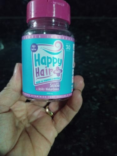 Cliente segurando um pote do suplemento Happy Hair com rótulo azul e tampa rosa.