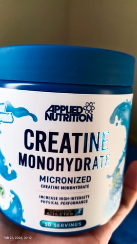 Close-up of a customer holding the blue tub of Applied Nutrition Creatine Monohydrate, showing the product label.