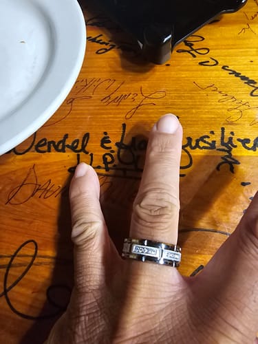 A close-up of a reviewer's hand wearing the Kaelen Ring on their finger, set against a wooden table with writing on it.