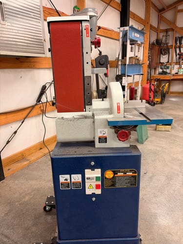 Customer's red EdgeCore Ceramic Sanding Belt installed on a large stationary belt grinder in a workshop setting.