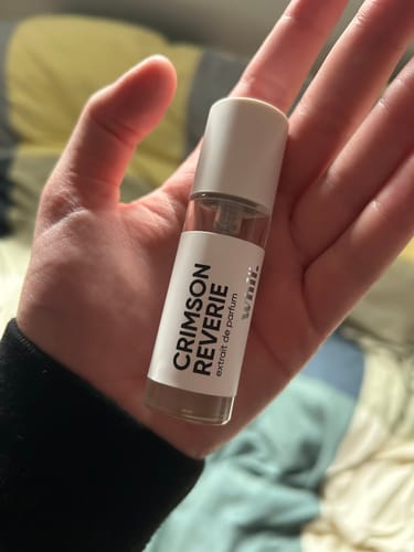 Customer holding the small glass bottle of Crimson Reverie perfume in the palm of their hand.