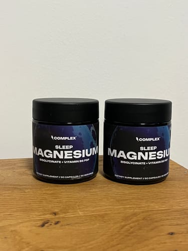 Reviewer's two black jars of Sleep Magnesium supplement on a wooden nightstand.