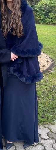 Cliente portant la cape châle bleu marine avec sa garniture en fausse fourrure sur une robe longue.