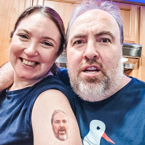 Customer showing a custom photo face temporary tattoo on her arm of the man beside her, who looks on with a funny expression.