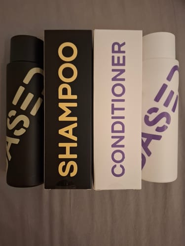 Customer's Shower Duo shampoo and conditioner bottles, one black and one white, displayed next to their matching boxes.