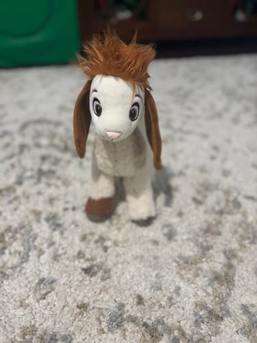 Customer's white Tali Plushie with fluffy orange hair standing on a grey carpet.