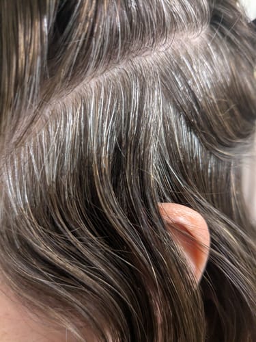 Close-up of a reviewer's dark hair, showing gray strands at the roots before using Grey Cover.