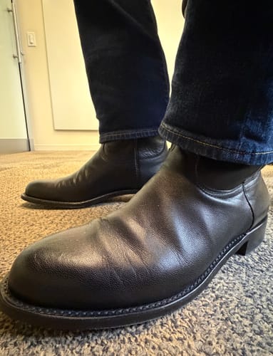 Close-up of a customer wearing the black leather Majestic Roper Western Boots with dark jeans indoors.