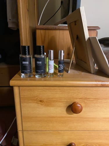 Customer's Smoke & Mirrors Eau de Parfum bottles and two rollerballs arranged on a wooden dresser.