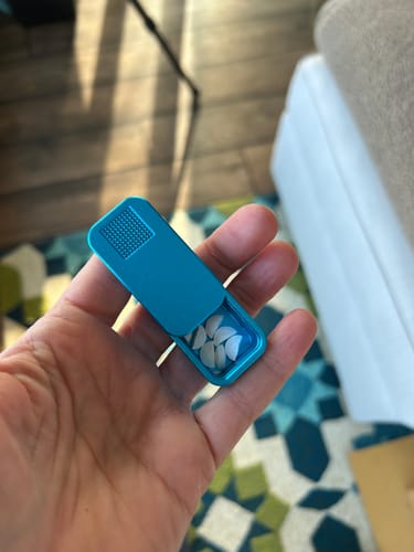 Customer holding a compact, teal metal pill case in their palm, open to show split pills inside.