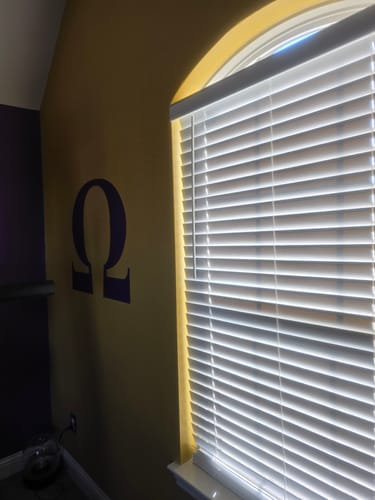 Customer's purple Omega Greek Letter Decal applied to a gold wall next to a bright window.