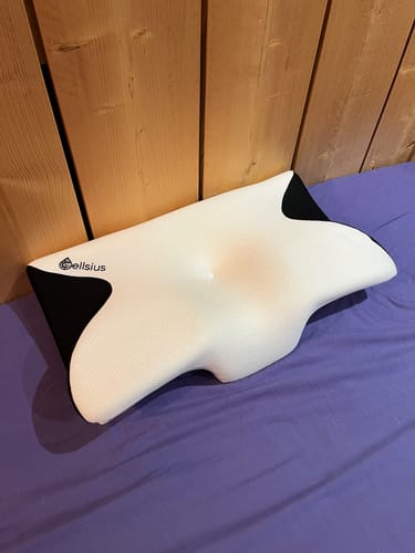 Le coussin d'alignement cervical Cellsius d'un client, posé sur un lit avec un drap violet.