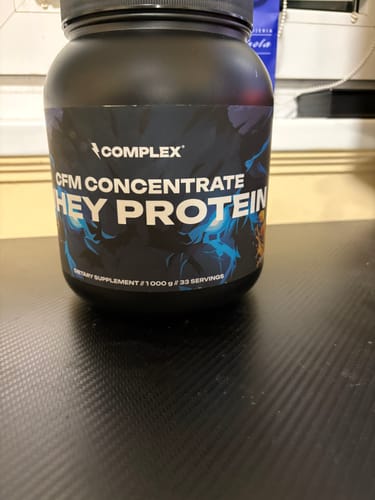 Customer's black tub of Complex CFM Concentrate Whey Protein sitting on a dark textured desk.