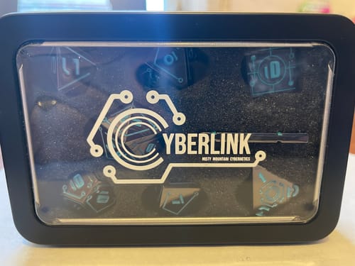 Customer's Cyberlink Void Blue Dice Set inside its black metal storage tin with a clear window.