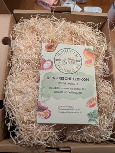 Kundenbewertung: Geöffnete Obstbox "Andalusien" mit schützender Holzwolle und einer Broschüre.