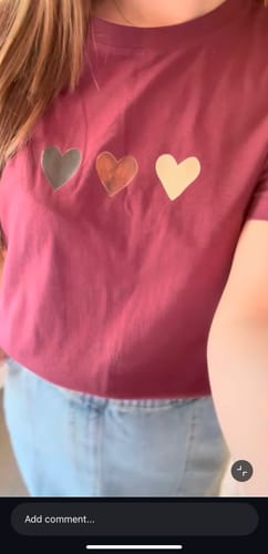 A reviewer wearing a maroon Everyday tee with a graphic of three hearts in silver, copper, and cream.