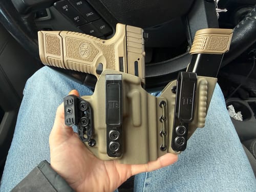 Customer holding their tan AXIS ELITE holster with a pistol and magazine, sitting in a car.