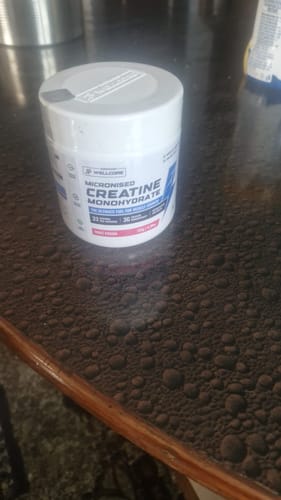 Customer's sealed white tub of Wellcore Micronised Creatine Monohydrate on a dark tabletop.