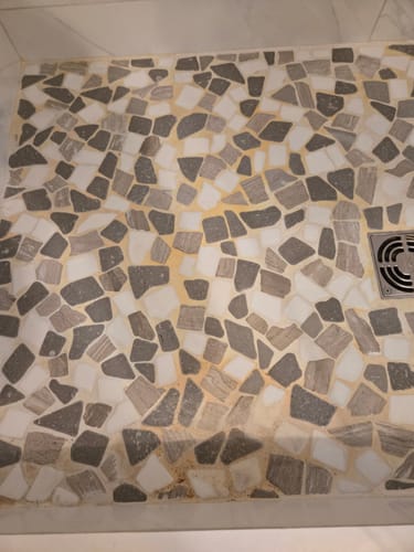 Close-up of a reviewer's stained mosaic tile shower floor before using the cleaner.
