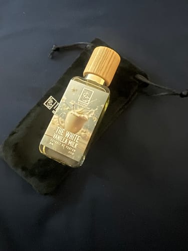 Reviewer's The White Vanilla Milk perfume bottle with a wood-grain cap, resting against its black velvet pouch.