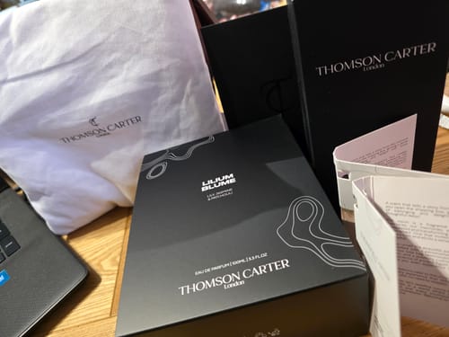 Reviewer showing the elegant black packaging for Lilium Blume perfume, alongside a branded bag and boxes.