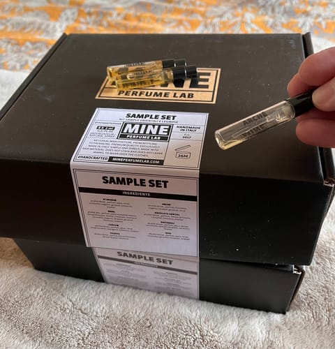 La mano di un recensore tiene una fiala del Set campioni fresche e pungenti sopra la scatola nera.