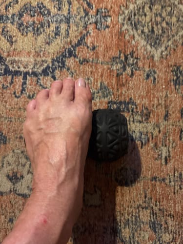 Customer rolling their foot over the black, textured Vibit ROLL massage roller.