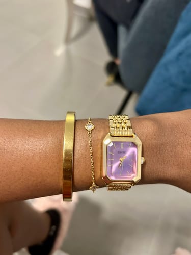 Customer wearing the gold CLAIRE DE MAINS watch with a purple face, styled on their wrist with a matching bangle and bracelet.