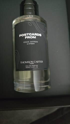 Customer's clear glass bottle of Postcards From | Eau de Parfum with a black cap and label.