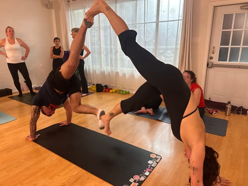 Reviewer in a yoga studio doing an inverted couples pose while wearing the black Halter Onesie, showing its open-back design.