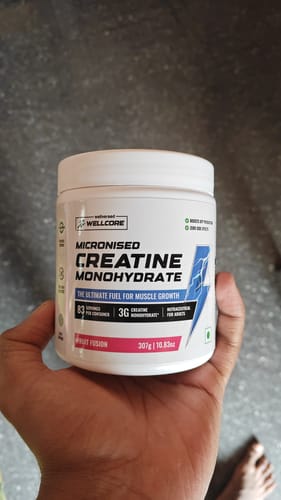 A customer holds a white container of Wellcore's Fruit Fusion Creatine Monohydrate in their hand.