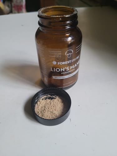 Customer's open amber jar of Lion's Mane Mushroom powder with a serving of the fine powder resting in the black lid in front.